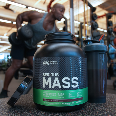 a tub of optimum nutrition serious mass with woman working out in background