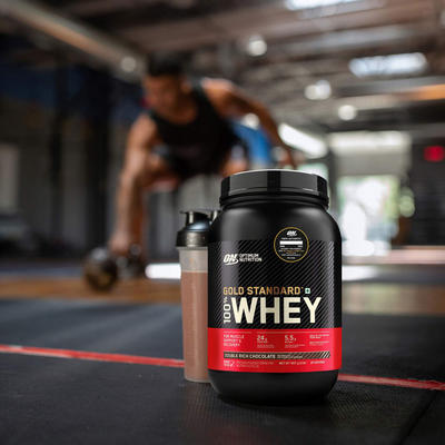 tub of optimum nutrition gold standard whey protein with a man training behind the tub